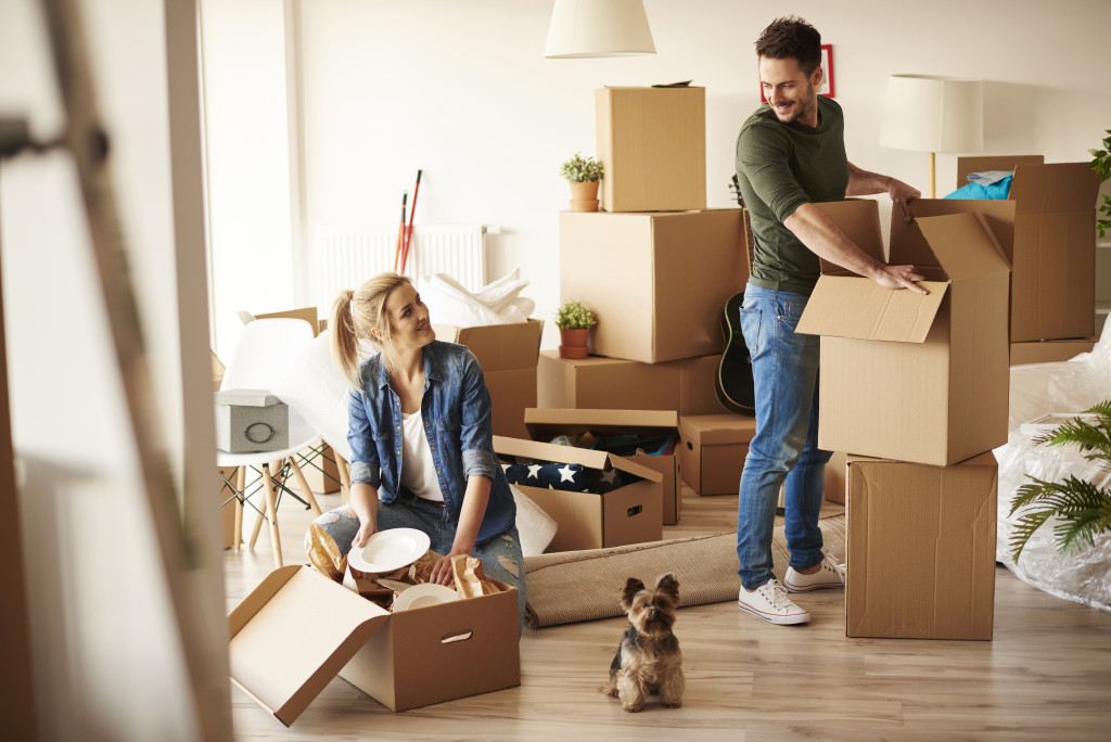 a couple smiling at each other while unpacking things in their new home with their dog between them
