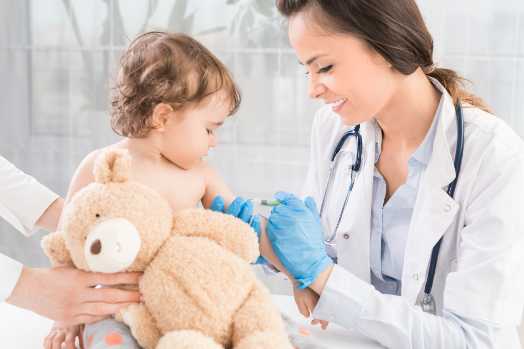 A pediatrician performing a vaccination on a little girl holding a teddy bear